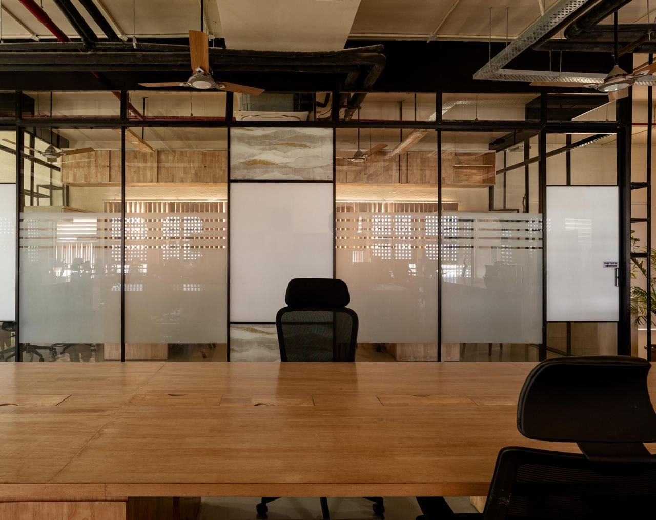 Black steel-framed glass partitions seen across a wooden table. The glass carries frosted bands, and two narrow panels hold a pattern of pale hills with gold lines.