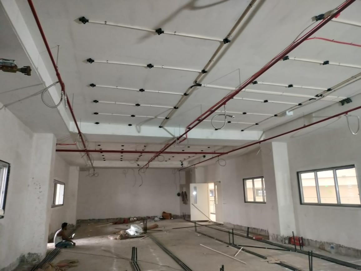 Site photograph, May 2025: the empty floor, with bare white walls and columns, and pipes and conduit running across the ceiling.