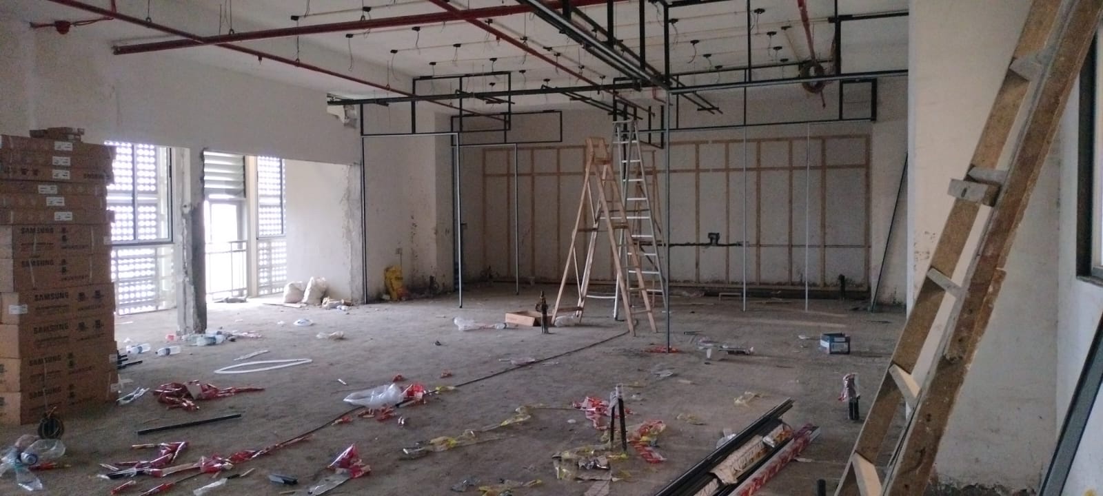 Site photograph, July 2025: black steel framing for the partitions standing on the bare floor, with two ladders beside it.